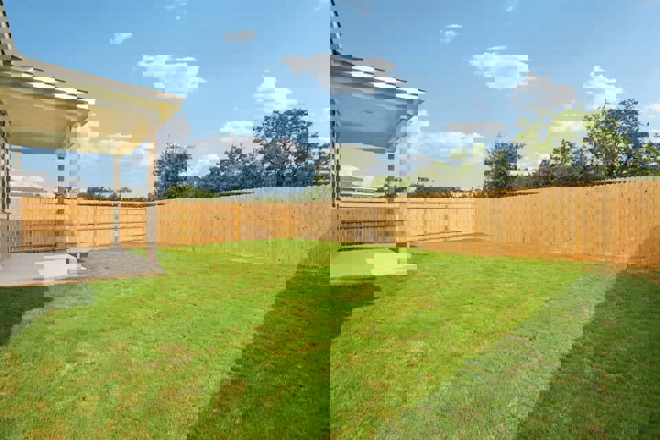 A fenced in yard with a wood fence and trees in the background.