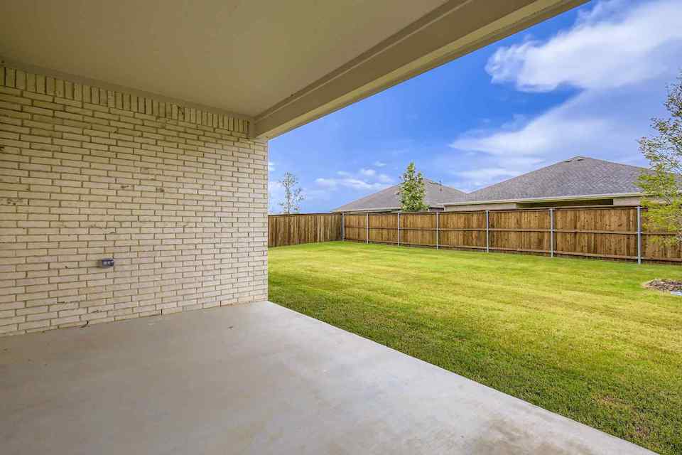 A fenced in yard with a brick wall and a grass field.