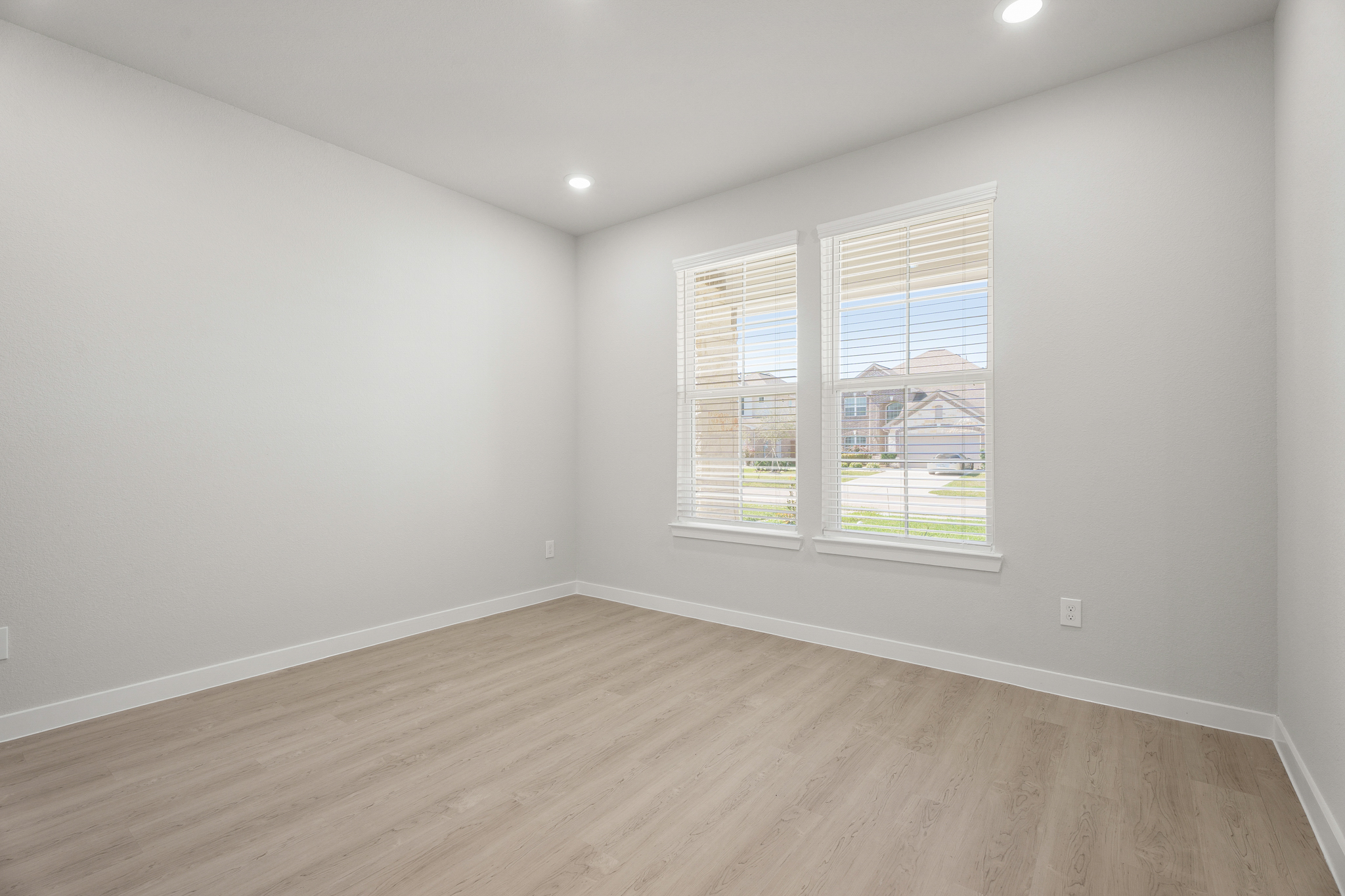 A room with a wood floor and a window with blinds.