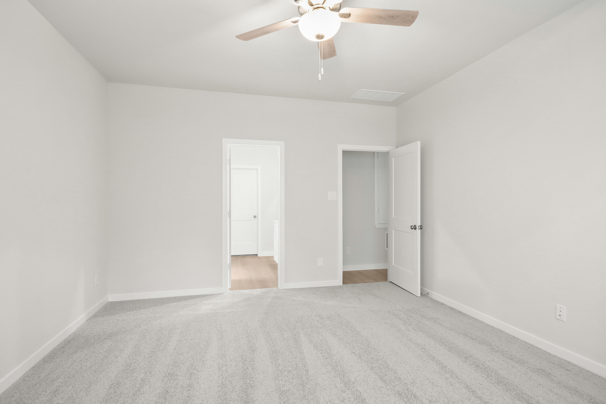 A room with a ceiling fan and a carpet.