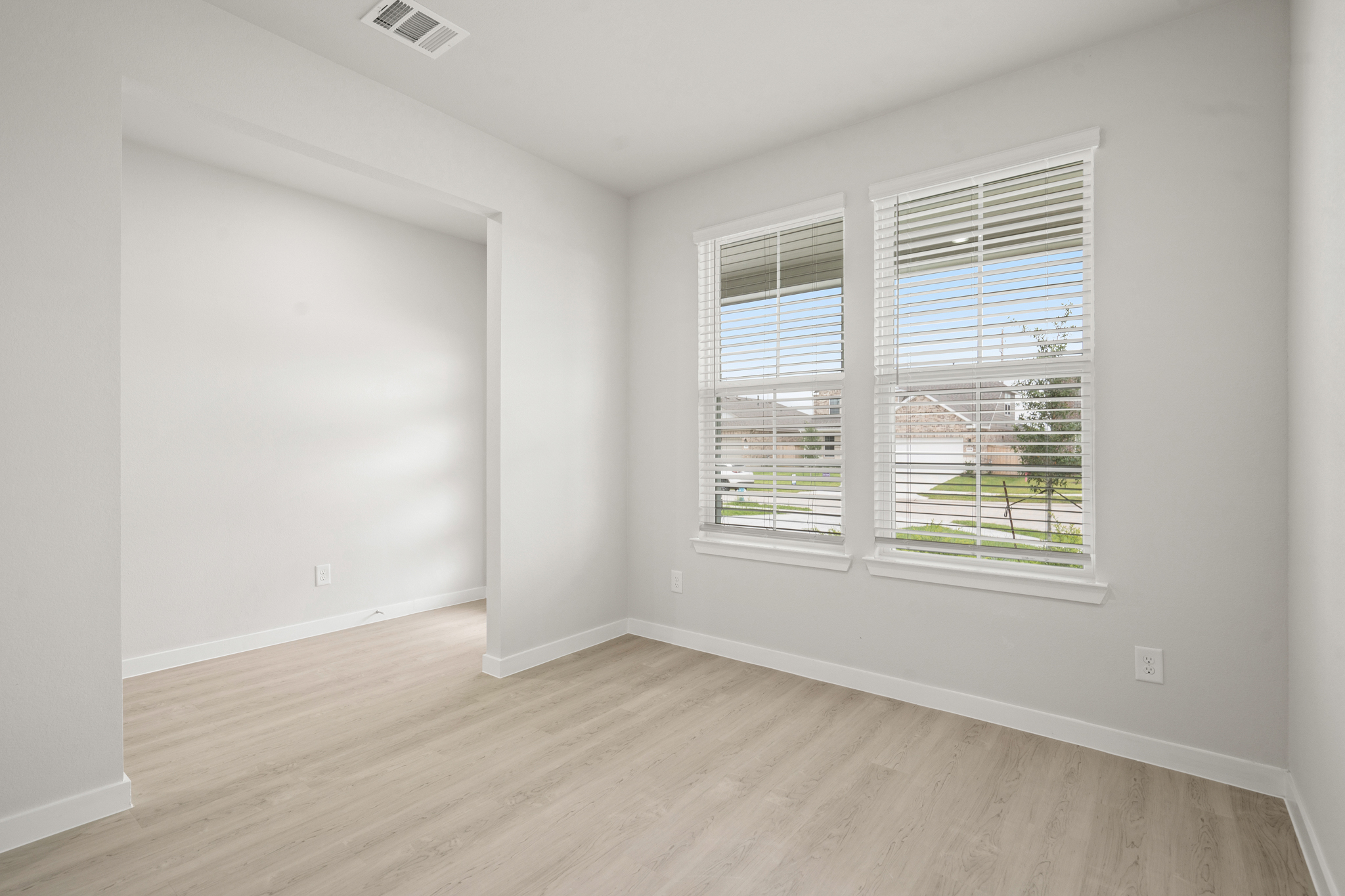 A room with a wood floor and a window with blinds.