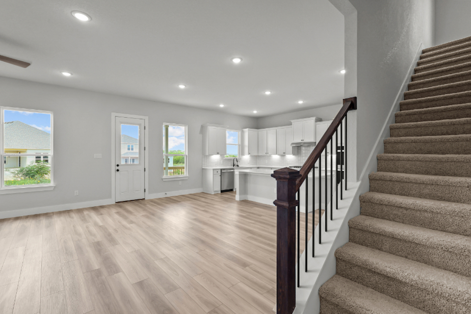A large white room with a wood floor and a wood staircase.